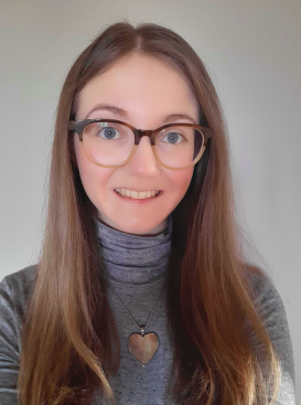 A headshot of Martha smiling. She wears large square glasses and a grey top